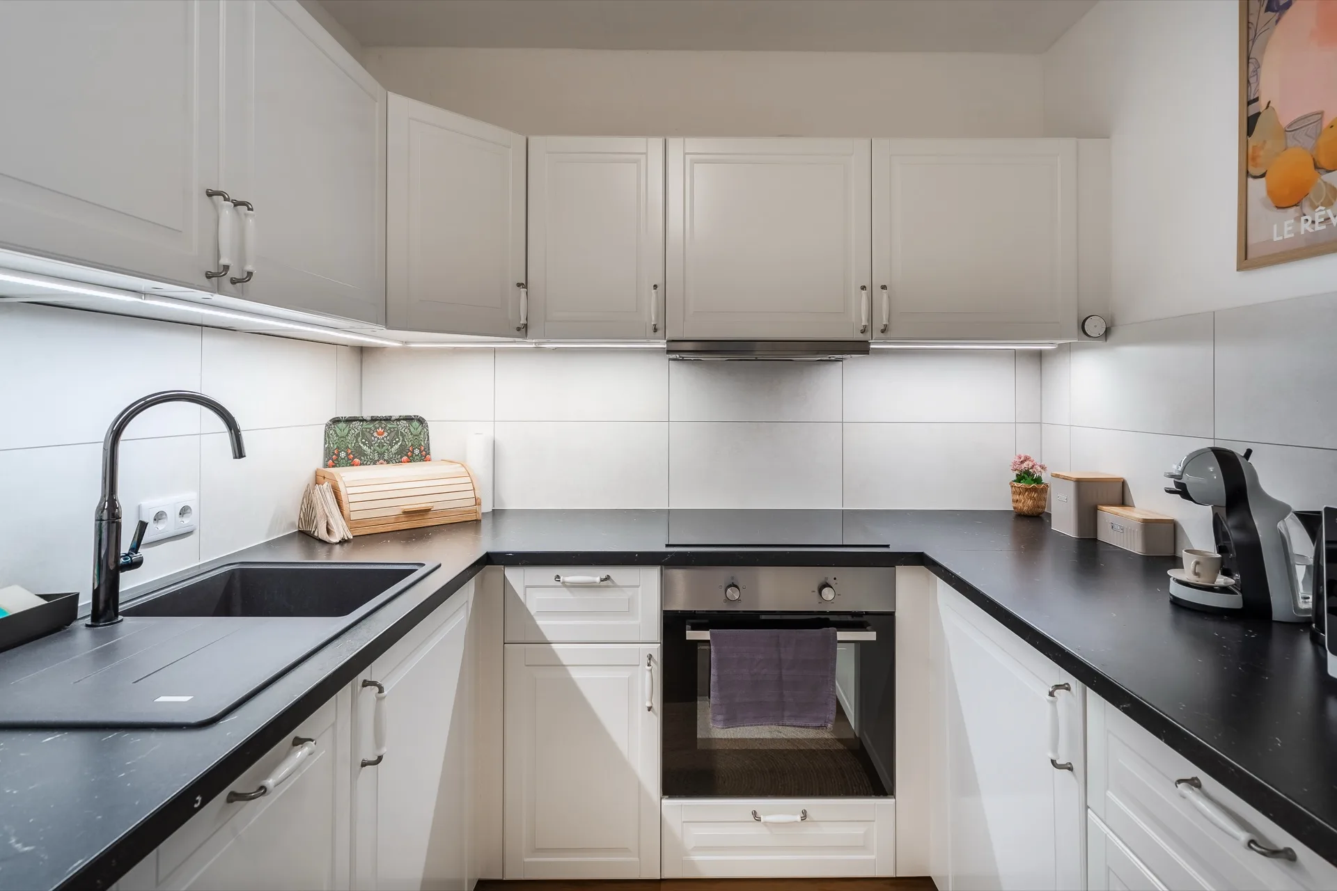 Vollausgestattete weiße Einbauküche mit schwarzer Arbeitsplatte, Backofen, Nespresso-Maschine und Herdplatten im Rosie Design Chalet Brunnach Bad Kleinkirchheim – Küchenfotografie Ferienwohnung Kärnten – Mathias Prägant Photography
