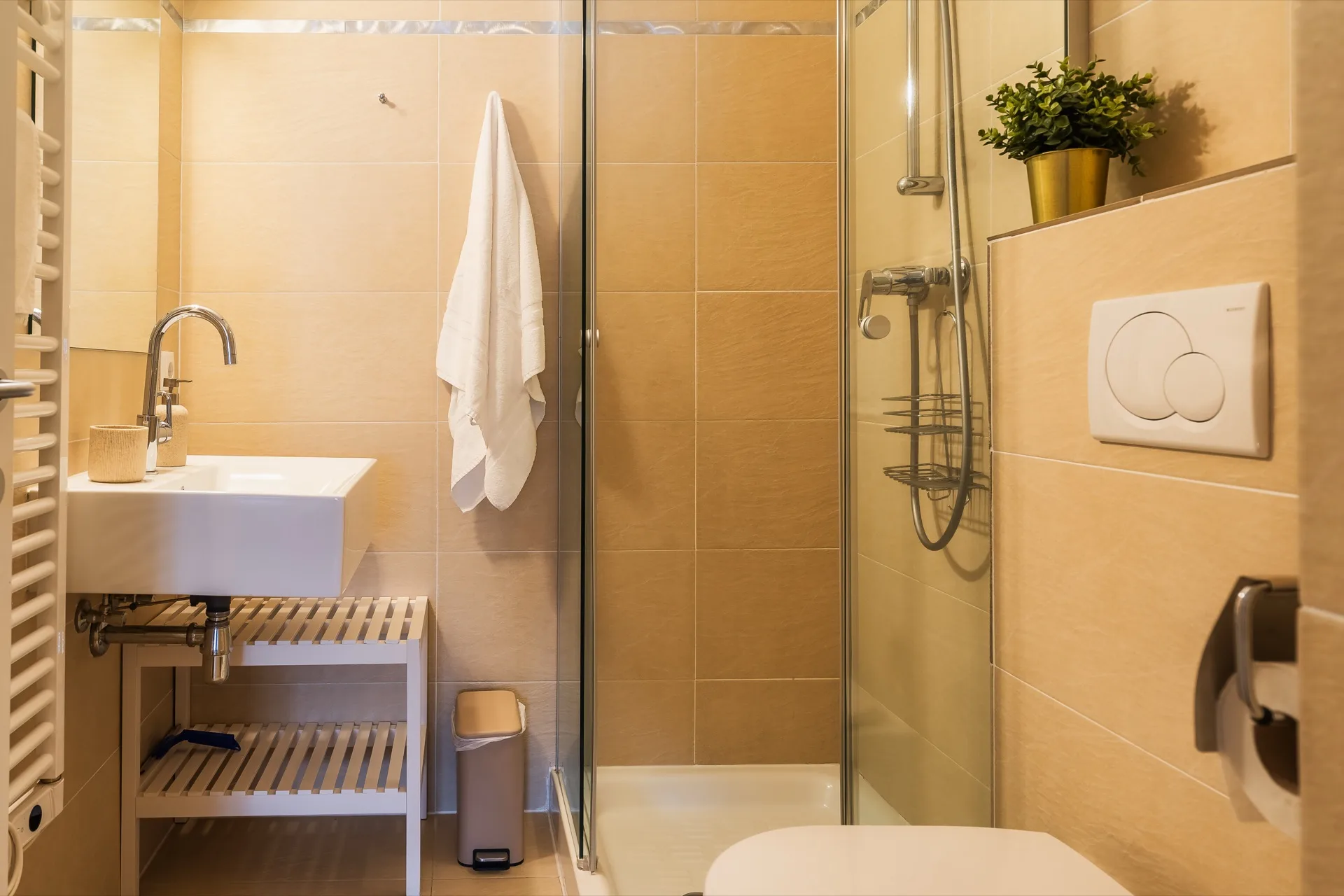 Badezimmer mit ebenerdiger Glasdusche, Waschbecken auf Holzablage, beigen Fliesen, Handtuchheizkörper und kleiner Pflanzendeko beim Rosie Design Chalet Brunnach Bad Kleinkirchheim – Badezimmerfotografie Ferienwohnung Kärnten – Mathias Prägant Photography