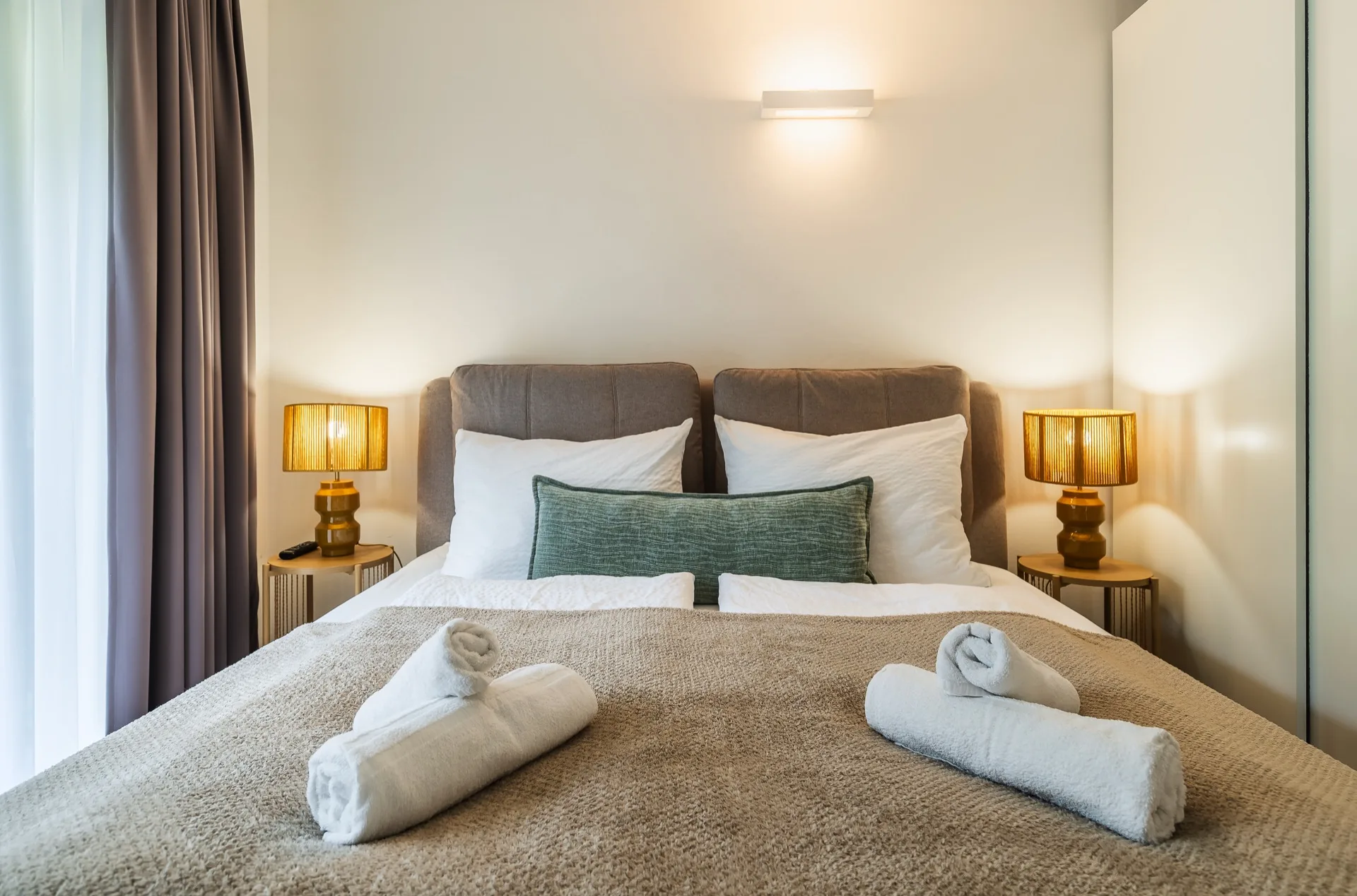 Elegantes Schlafzimmer mit Boxspringbett, goldenen Nachttischlampen, weißer Bettwäsche und gerollten Handtüchern im Rosie Design Chalet Nockalm Bad Kleinkirchheim – Schlafzimmerfotografie Ferienwohnung Kärnten – Mathias Prägant Photography