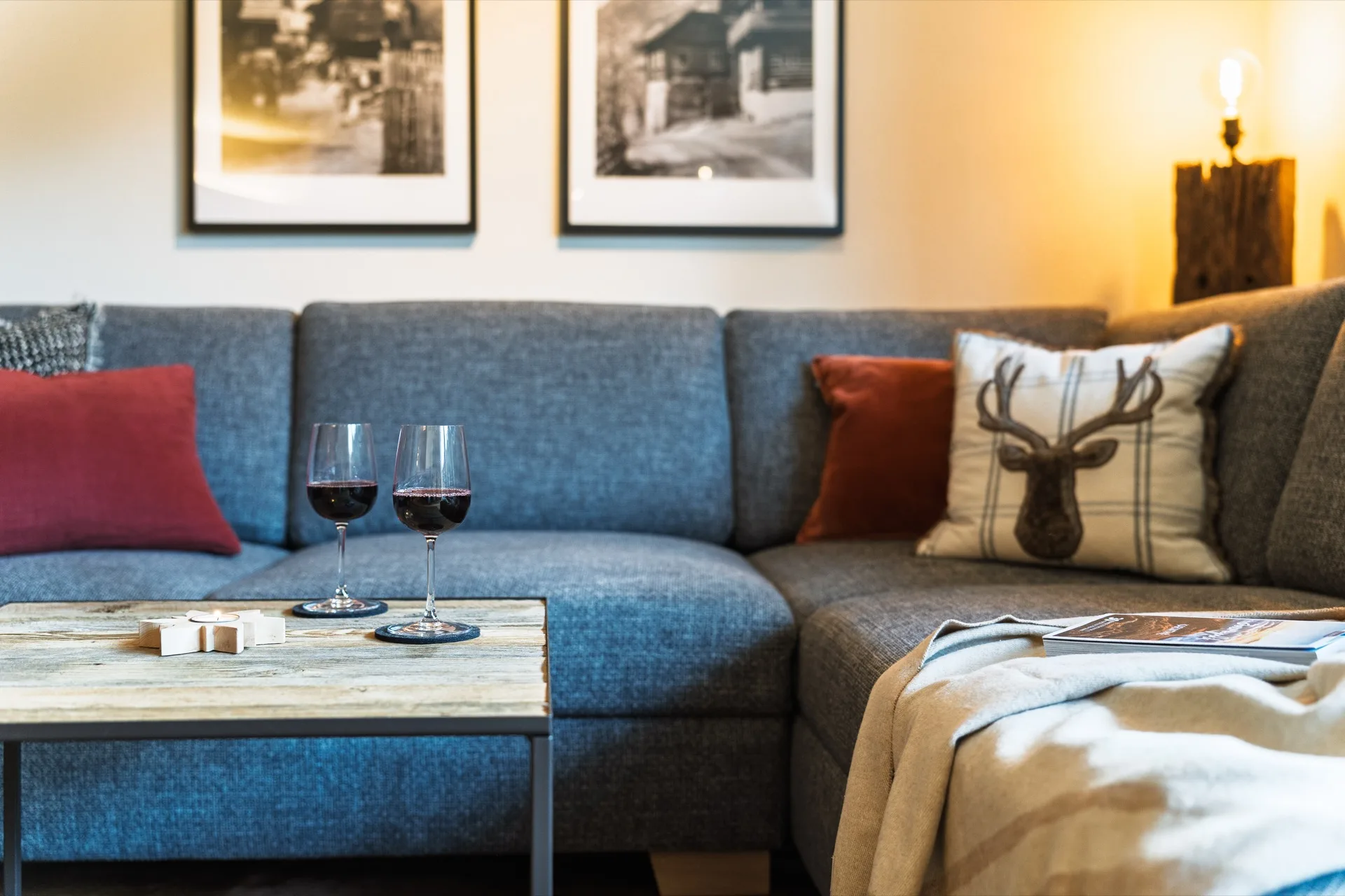 Stimmungsvoller Sofa-Ausschnitt mit zwei Rotwein-Gläsern, Hirsch-Kissen und warmer Abendbeleuchtung in der Bergfreunde Bad Kleinkirchheim – Urlaubsgefühl pur – Mathias Prägant Photography