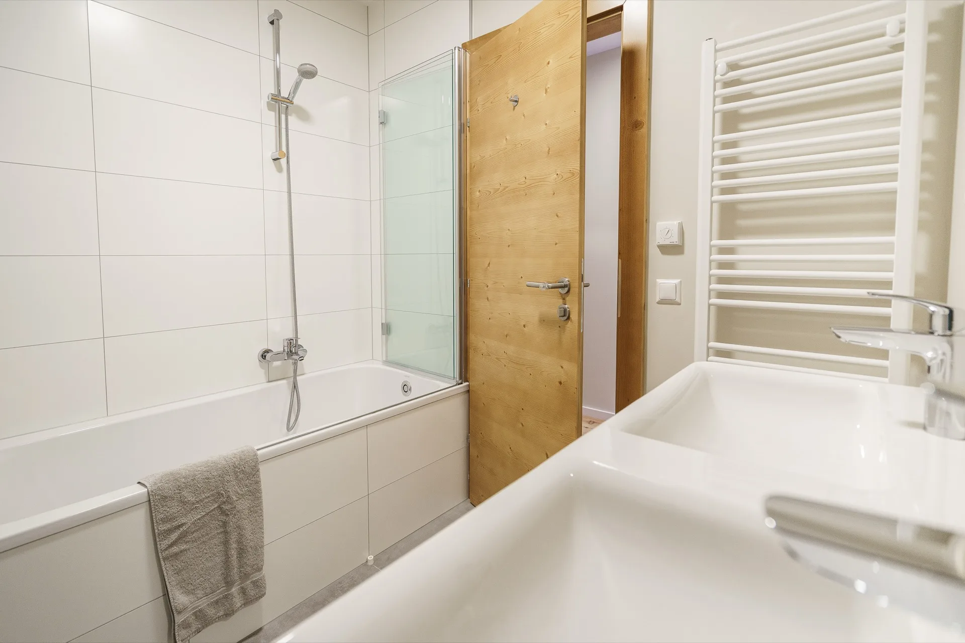 Modernes weißes Badezimmer mit Badewanne, Glasdusche, Doppelwaschbecken und Handtuchheizkörper in der Bergfreunde Bad Kleinkirchheim – Badezimmerfotografie Ferienwohnung – Mathias Prägant Photography