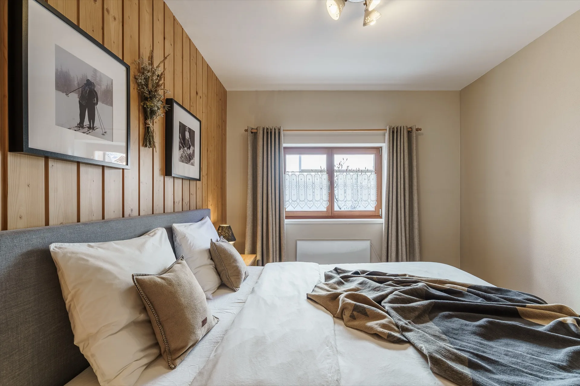 Helles Schlafzimmer mit Holzwandverkleidung, weißer Bettwäsche und Vintage-Ski-Wandfotos in der Bergfreunde Bad Kleinkirchheim – alpine Schlafzimmerfotografie – Mathias Prägant Photography