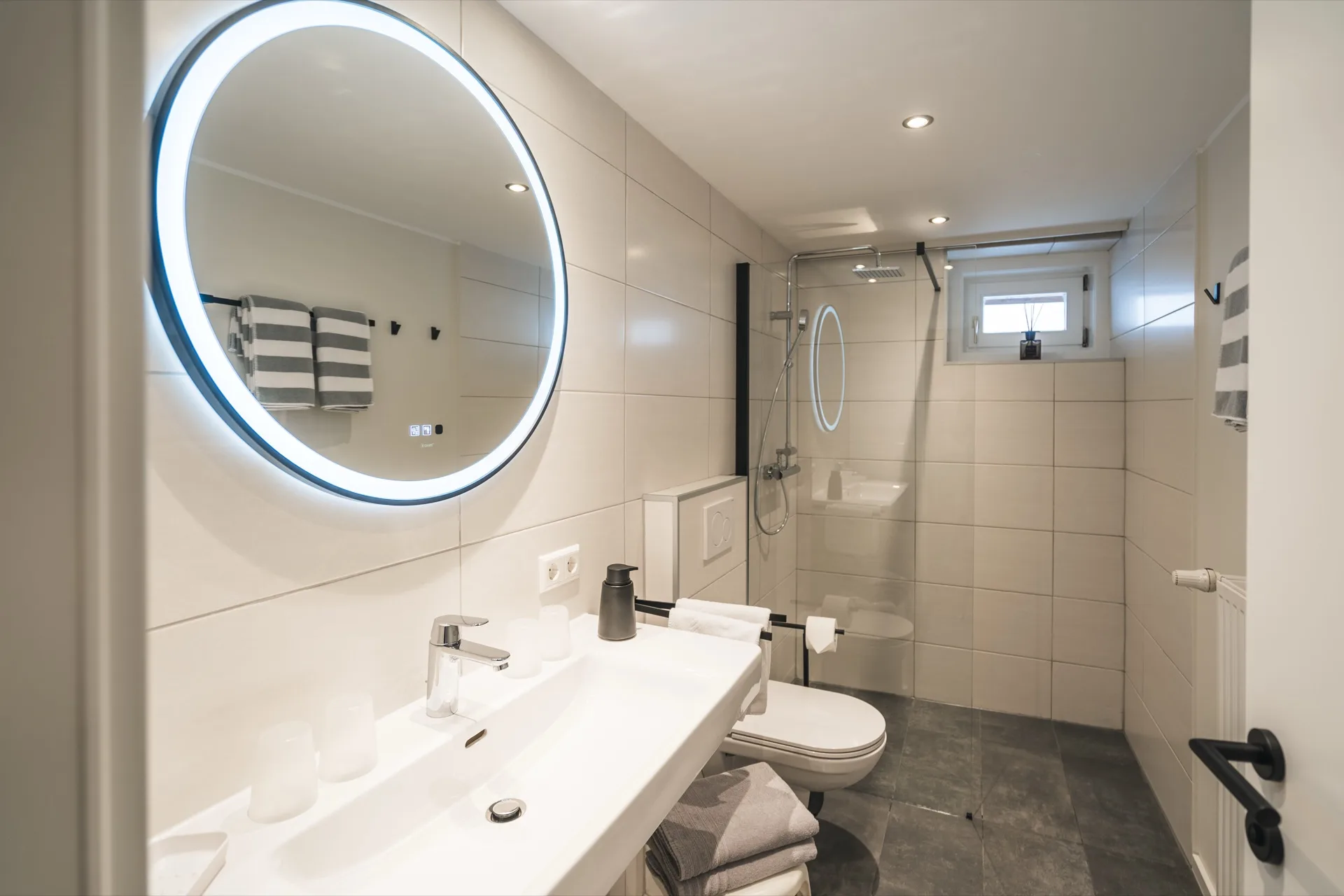 Modernes Badezimmer mit rundem LED-Spiegel, ebenerdiger Dusche und hochwertiger Ausstattung im Landhaus Apartments Prägant Bad Kleinkirchheim – Ferienwohnung Fotografie Kärnten